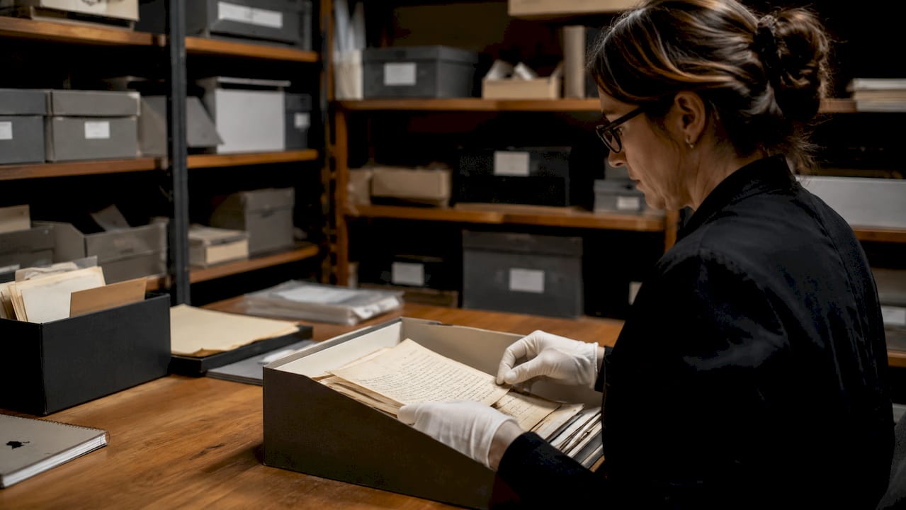 Hands placing documents into acid-free archival folder in climate-controlled vault